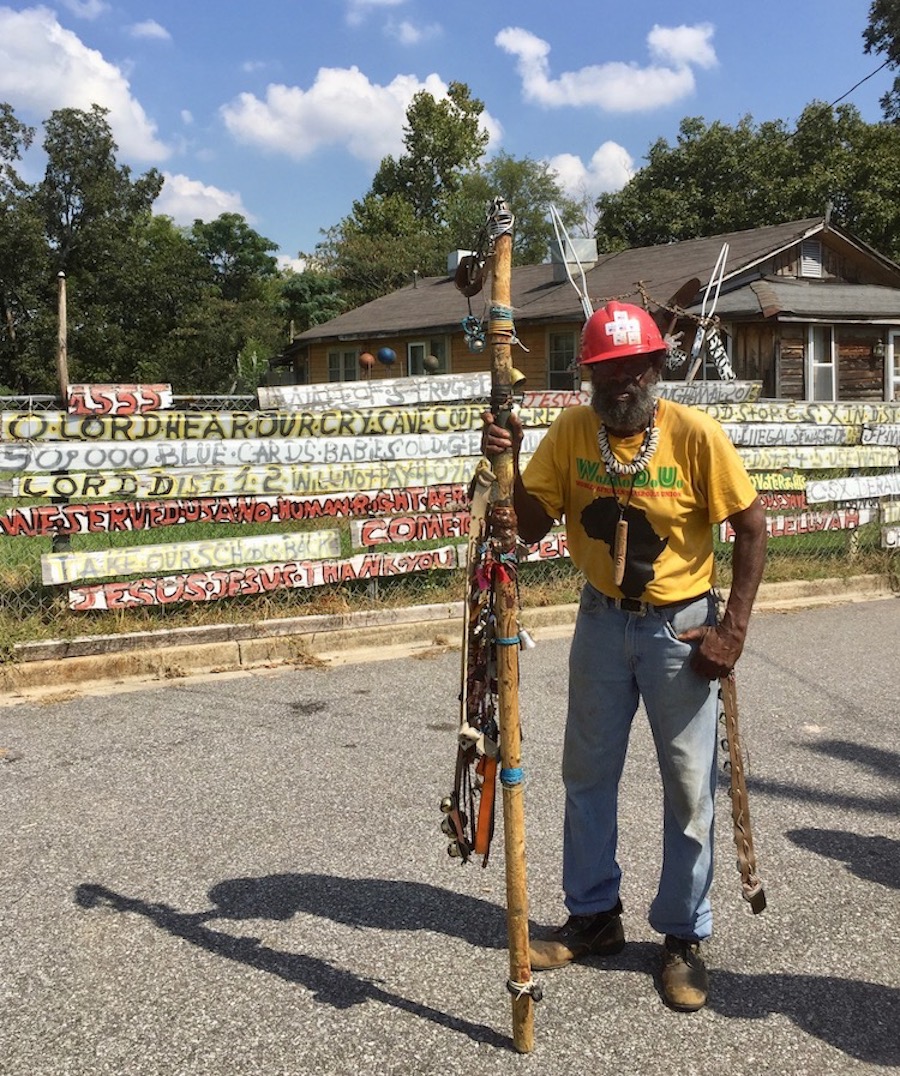 Folk artist in front of fence painted with slogans