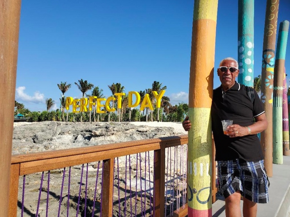 man leaning agains post on beach with perfect day sign on side
