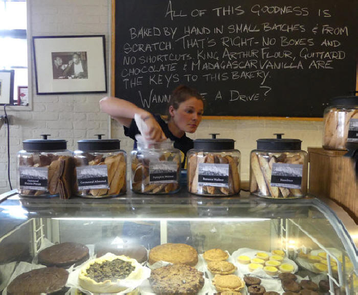 Enrico Biscotti clerk getts biscotti from jars above display case filled wiht baked goods