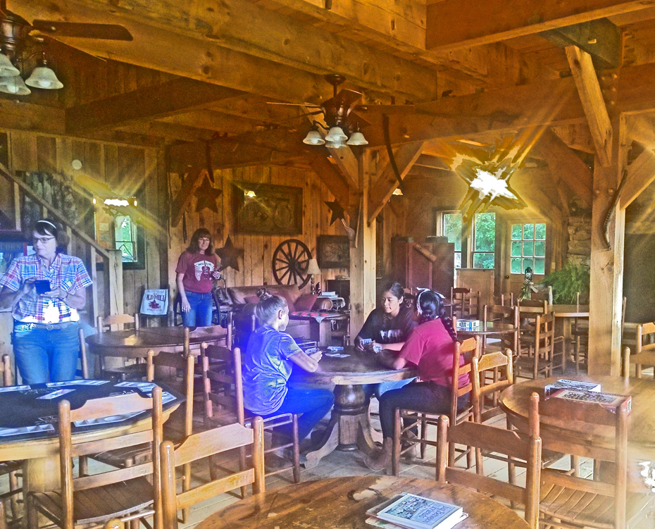 Three girls playing cards and two women watching in Iron Horse Saloon at French Broad Outpost Dude Ranch in Eastern Tennessee