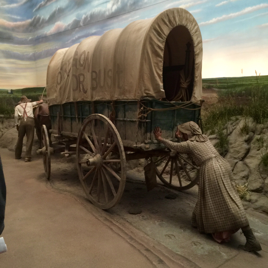 Pioneer husband and wife pushing awagon up a hill mural