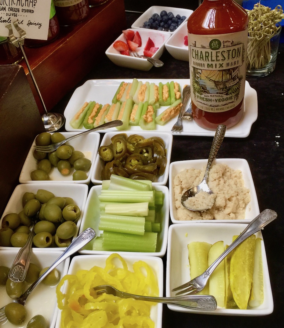 olives, celery, peppers and berries on brunch plate with bottle of bloody mary mix
