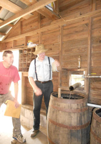 Twomen watchas turpentine flows from the still tubing into a barrel.
