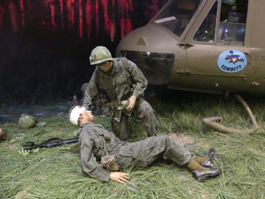 Medic aids wounded soldier exhibit with Cowboy helicopter in background